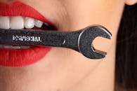 A close-up shot of red lips holding a shiny wrench with bold red lipstick.